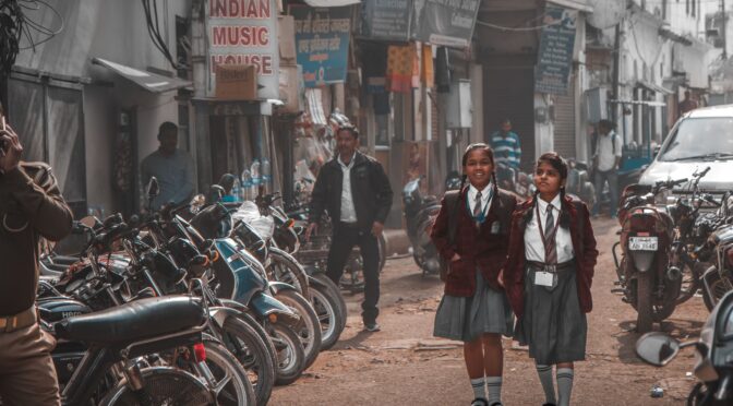 Two schoolgirls in uniform walking along a busy street in Amritsar, India.